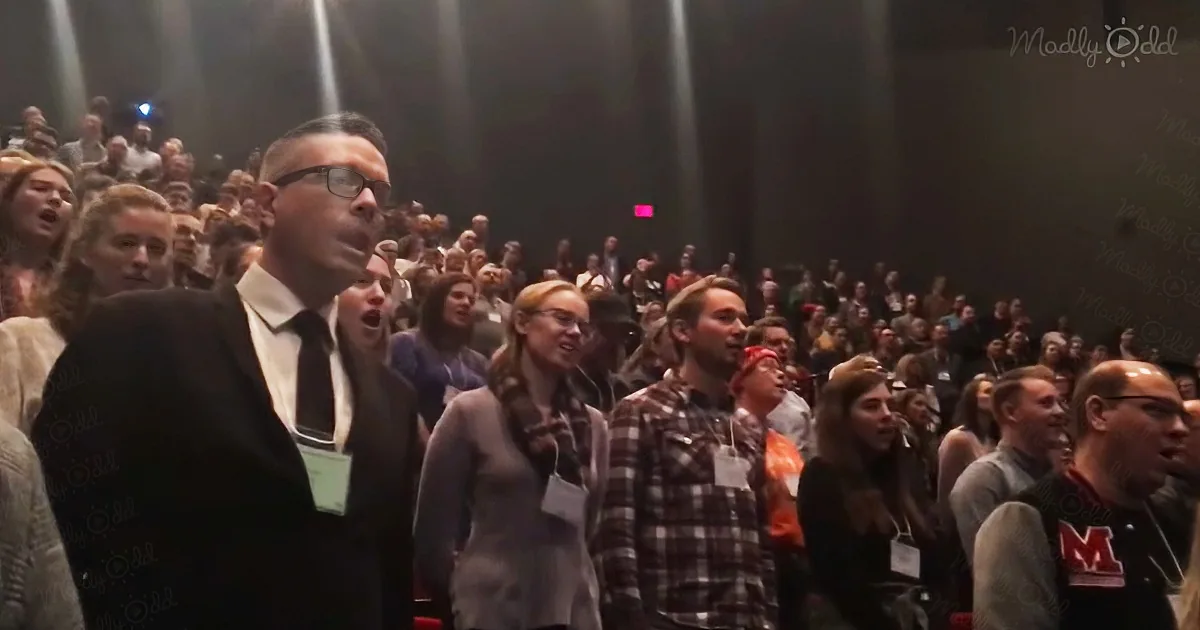 A man in a suit stands in a crowd, looking up with others reacting to something.