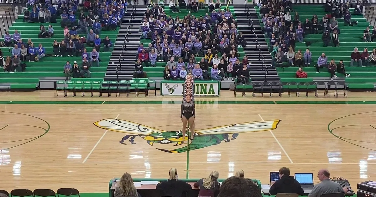 A cheerleading team in black uniforms performs a routine on a basketball court with a green and yellow logo.