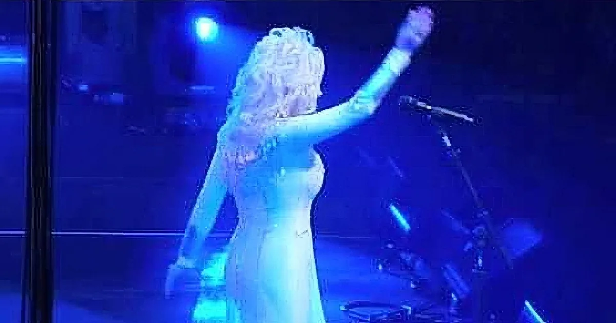 Dolly Parton sings on stage in a white dress under blue lighting.