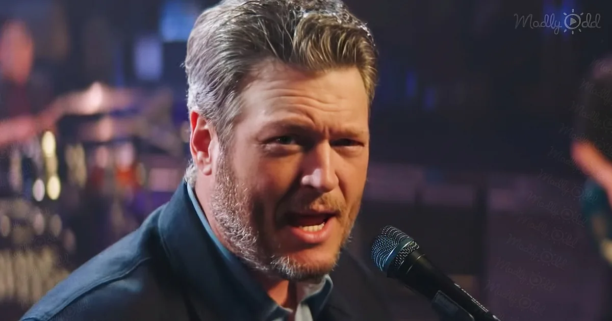 A man with short, styled hair sings into a microphone, wearing a dark jacket, with a blurred background and "Madly Odd"...
