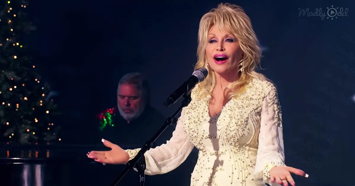 Dolly Parton sings on stage in a glittery dress, with a Christmas tree and a man playing piano in the background.