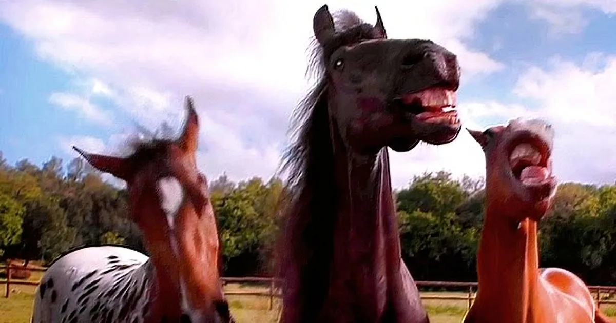 A horse with an open mouth stands between two other horses, all in a natural setting.