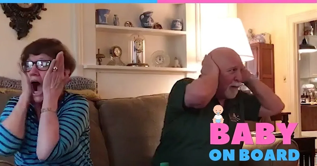 A woman in a striped shirt covers her face, laughing, while a man in a green shirt holds a phone, both seated on a couch.