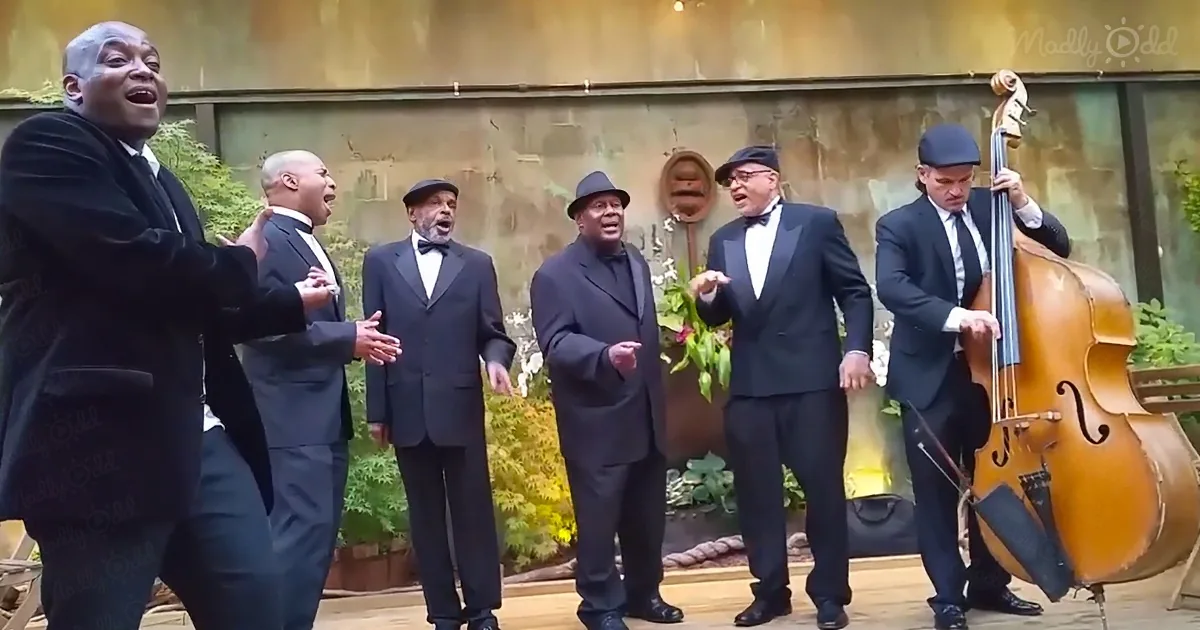 A group of men in suits and hats sing and play a double bass on a stage.