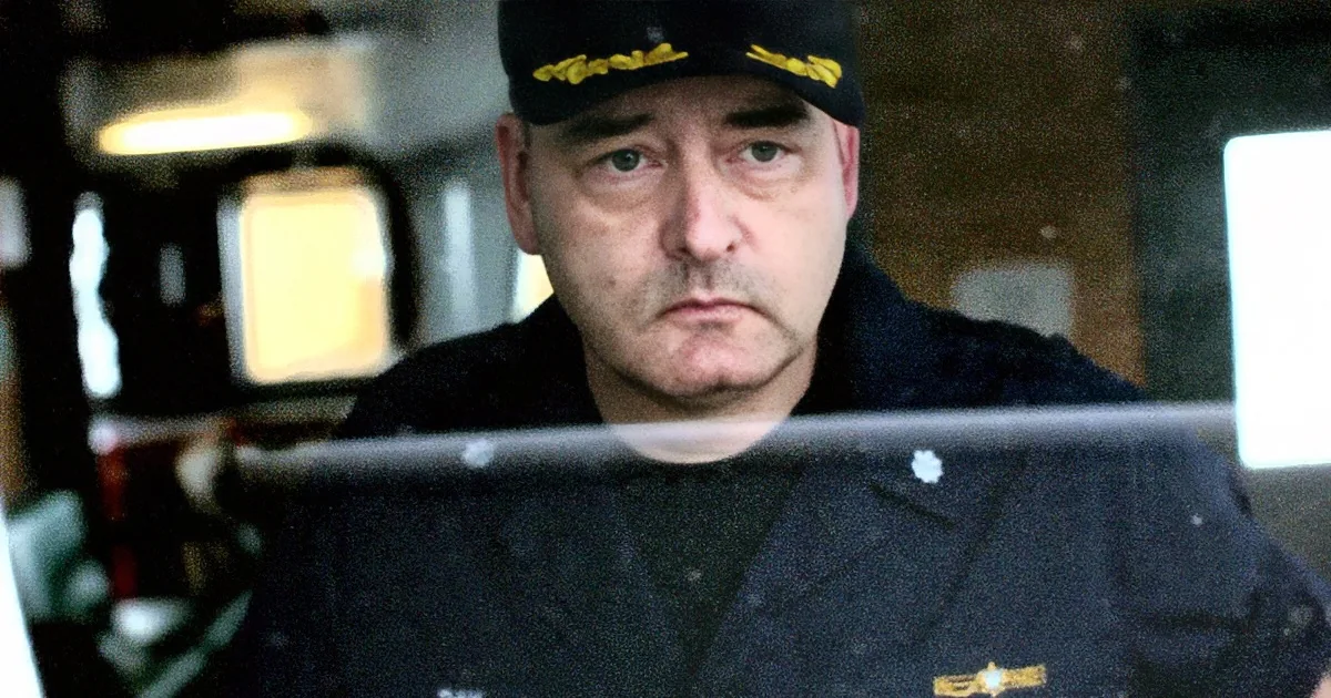 A man in a navy uniform and cap is focused on a laptop screen, with a blurred background.