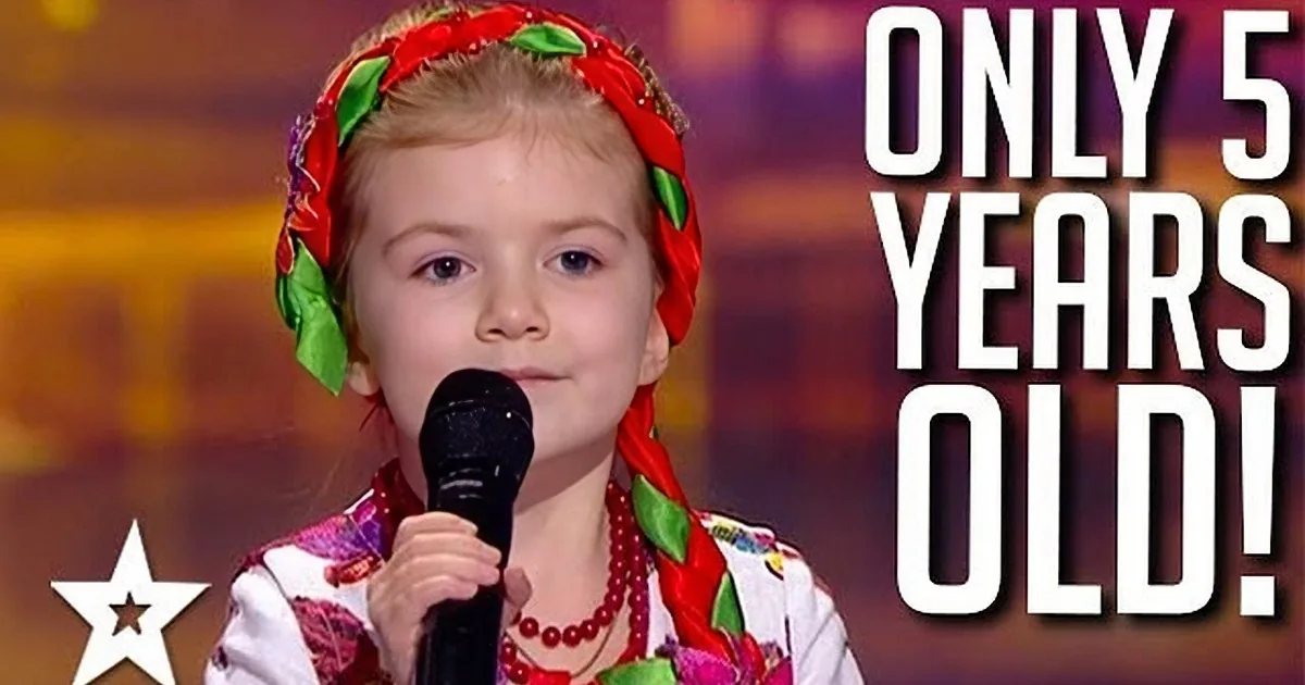 A young girl in traditional attire sings into a microphone on a stage.