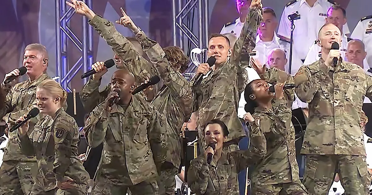 A group of military personnel in camouflage uniforms sing and perform on stage.
