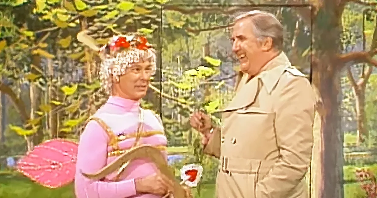 A person in a pink outfit with a red umbrella and a man in a beige trench coat are talking in a garden setting.
