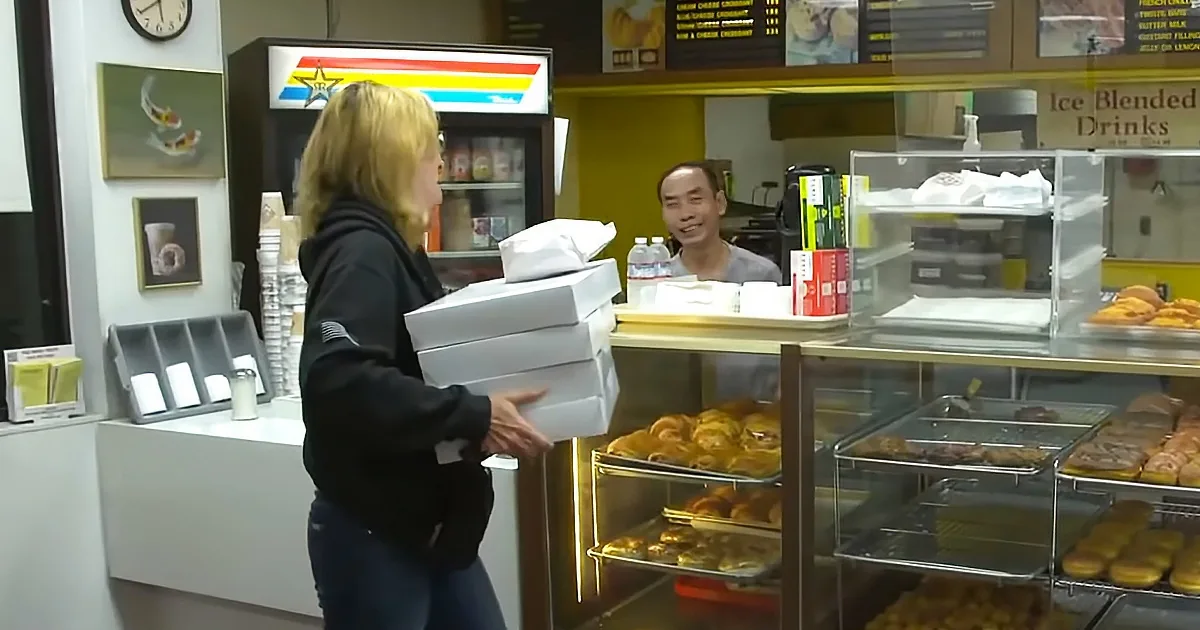 A woman carries three white boxes past a bakery display with pastries and drinks.