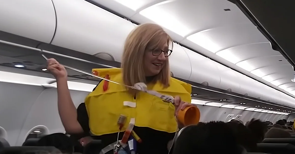 A flight attendant in a yellow vest is demonstrating safety procedures on an airplane.