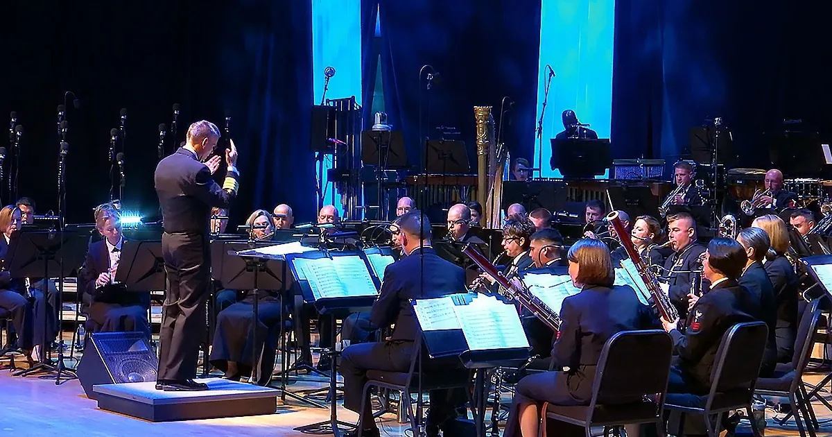 Conductor leads orchestra on stage with musicians and instruments.