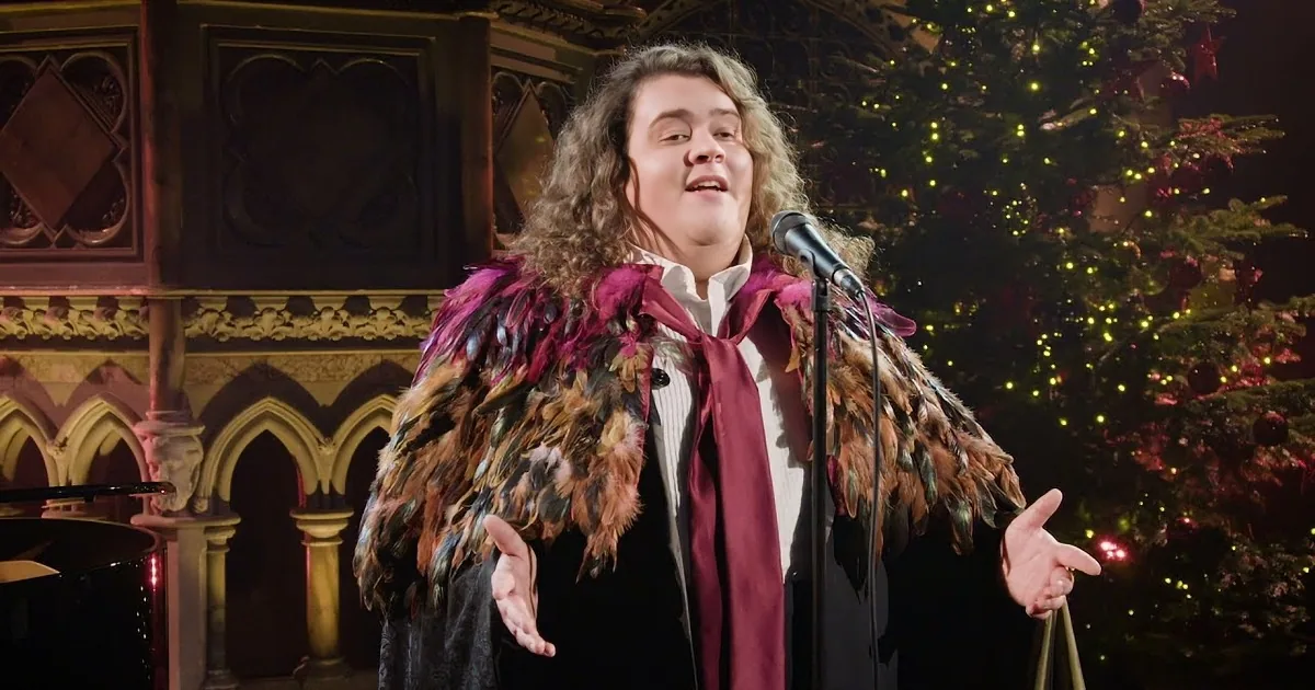 A person in a colorful feathered coat sings into a microphone on stage.