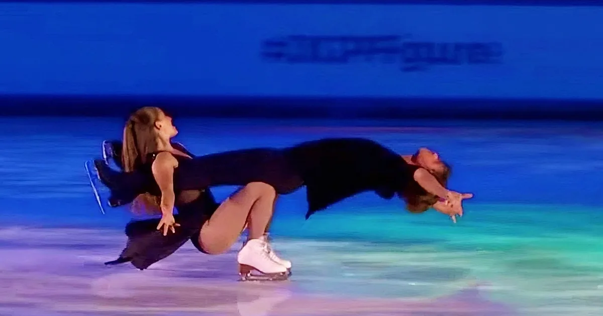 A figure skater in a black outfit is performing a dramatic pose on the ice.