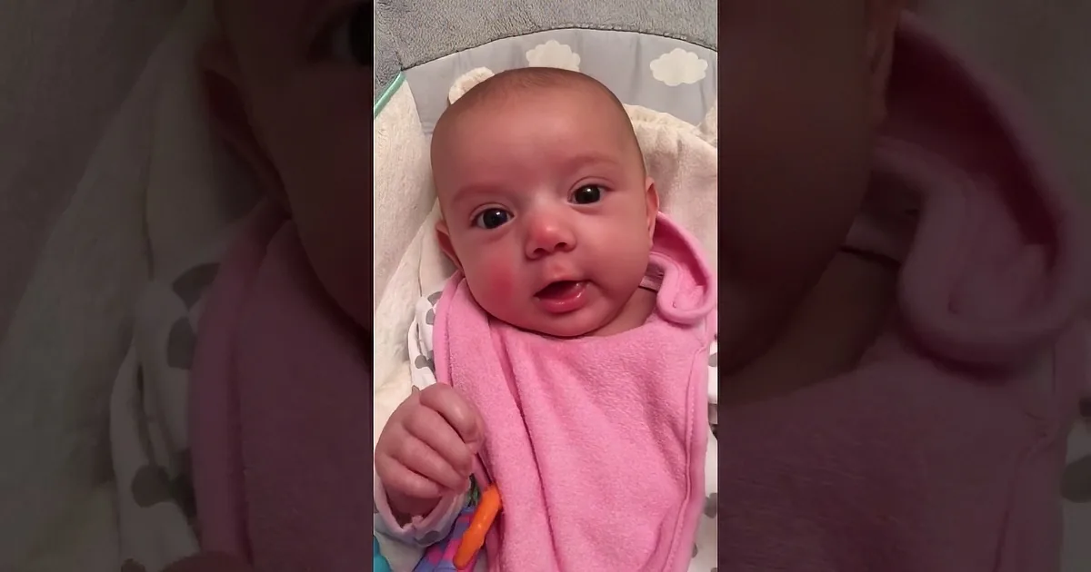 A baby wrapped in pink, smiling and looking directly at the camera in two close-up shots.