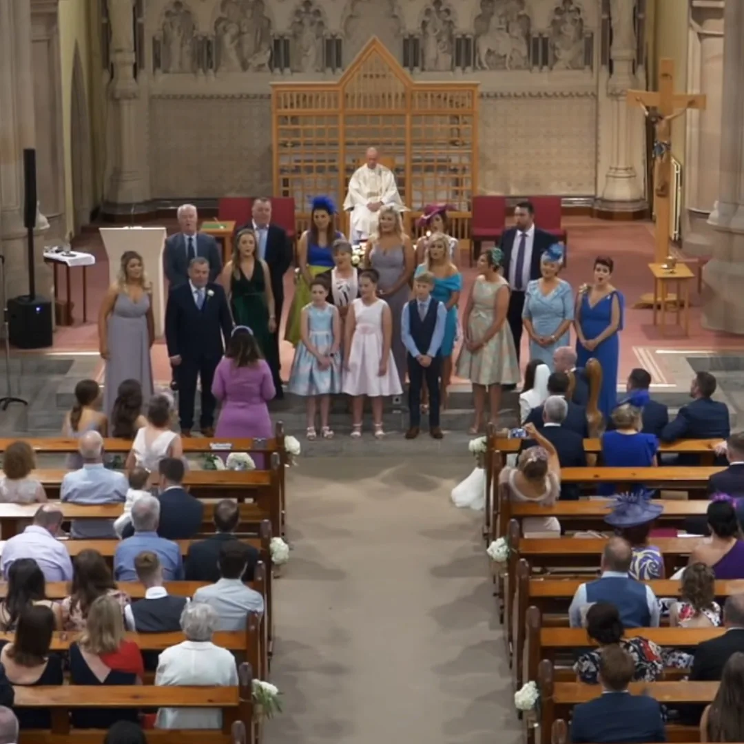 A wedding ceremony in a church with a priest, bridesmaids, and groomsmen standing on the altar.