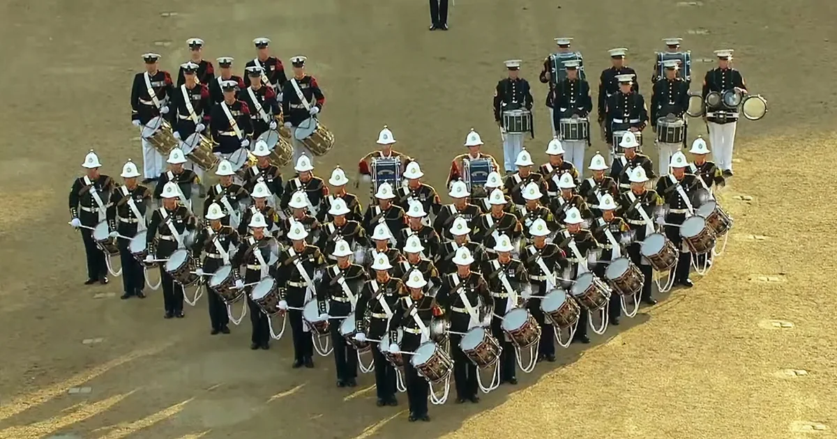 A marching band in uniform stands in formation, holding drums and instruments.