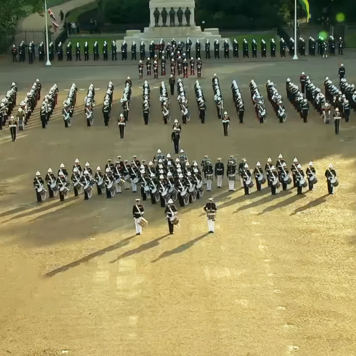 A military band in formation with drums and trumpets, marching in a large open area.