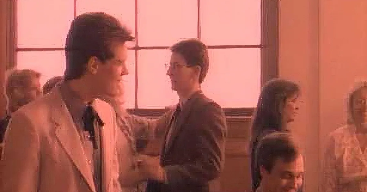 A man in a suit plays guitar while a group of people watch in a warmly lit room.