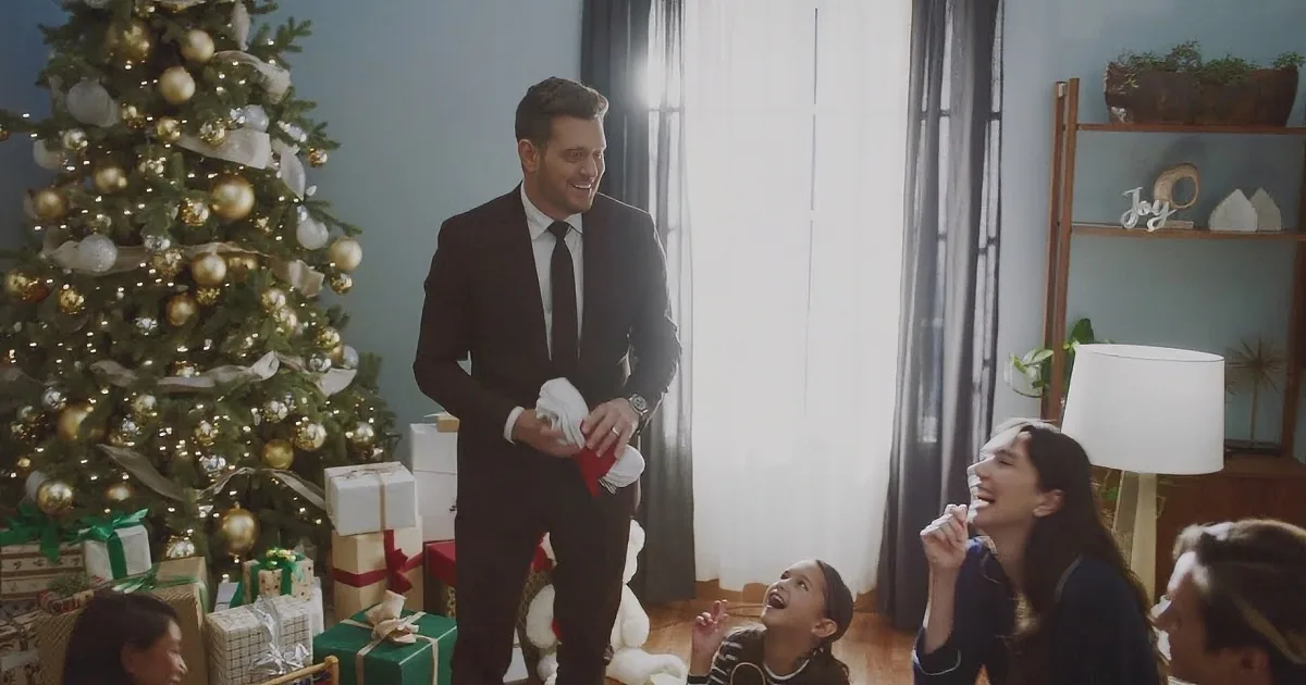 A man in a suit sings in front of a festive Christmas tree with lights.