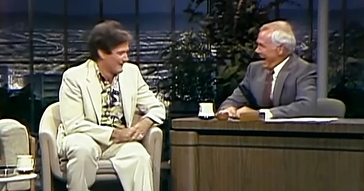 Two men in a studio setting, one in a light suit, the other in a suit and tie, engaged in conversation.