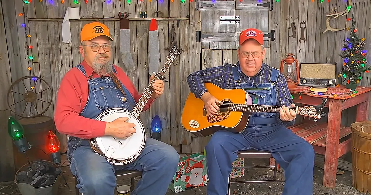 Two men play banjo and guitar in a rustic setting with Christmas lights and decorations.