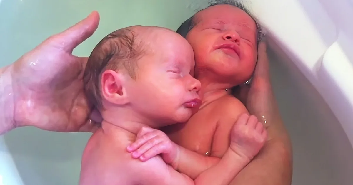 Two newborn babies are being bathed, one held by a hand, both appearing calm and peaceful.