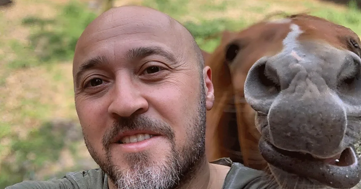 A man is affectionately kissing a horse, holding its head gently with both hands.