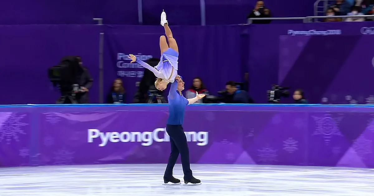 A figure skater in a blue outfit is being lifted by another skater on an ice rink at the PyeongChang 2018 Olympics.