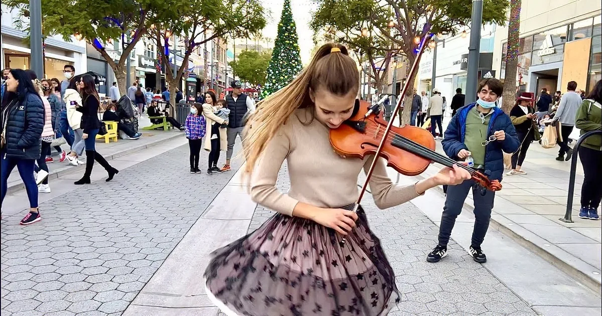 A young woman plays the violin on a city street, her hair flowing as she smiles.