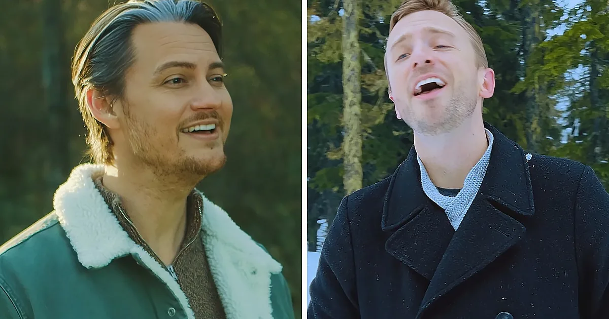 A man in a green jacket with a white fur collar sings outdoors, another man in a black coat sings nearby.