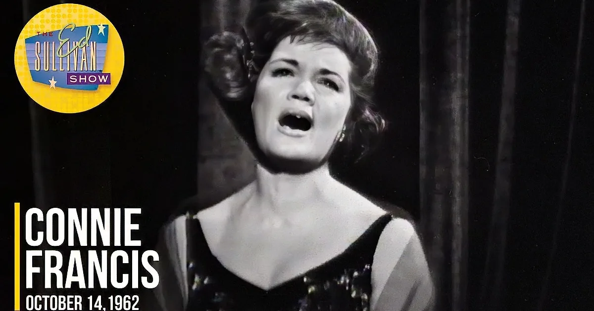 A woman in a black dress with a cape, arms outstretched, singing on stage.