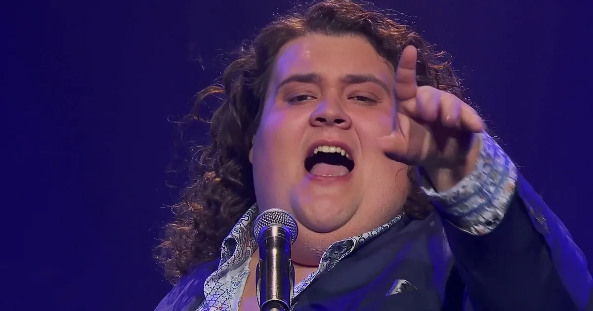 A man in a suit sings passionately on stage with arms outstretched, under blue lighting.