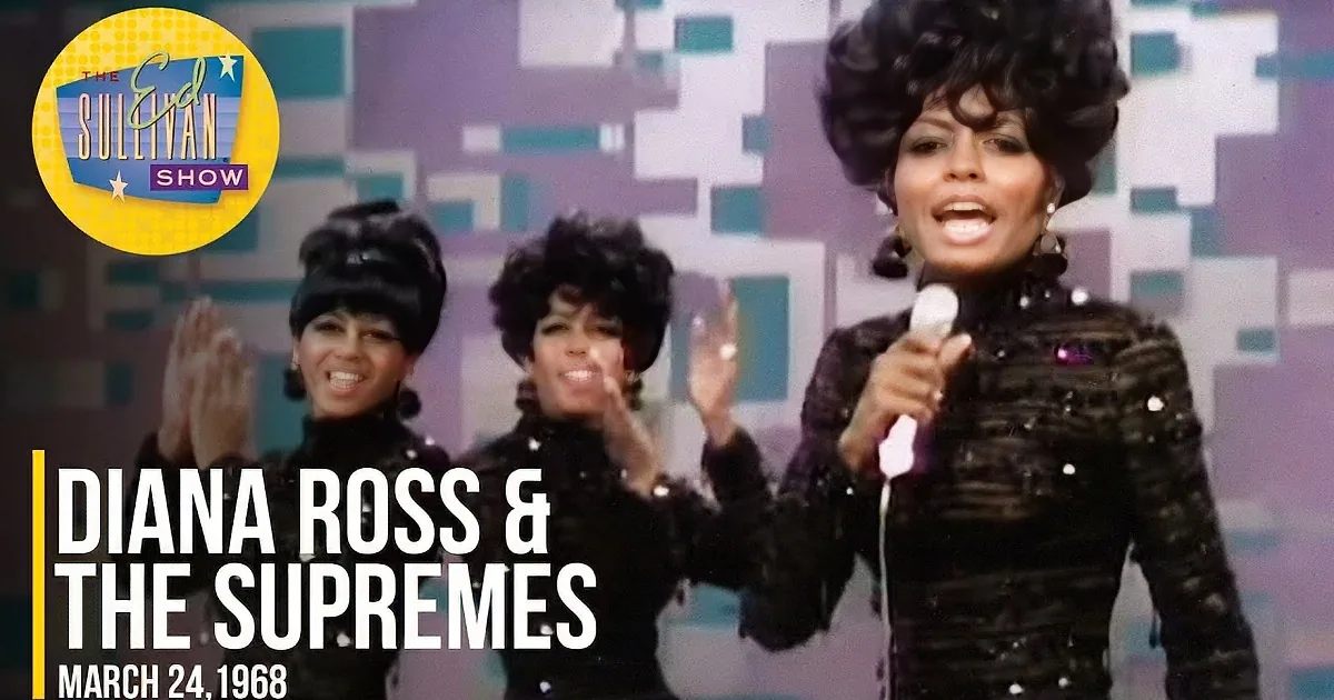 Three women in matching black sequined outfits perform on stage, smiling and singing.