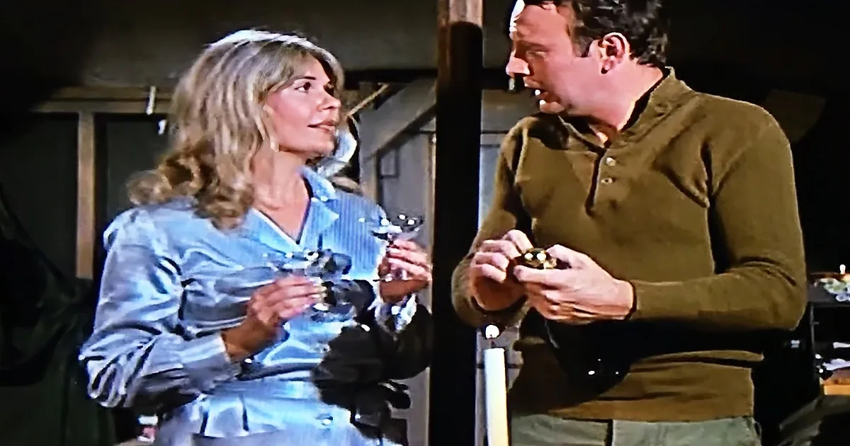 A woman in a blue dress holds a glass, while a man in a green shirt examines something in his hands.