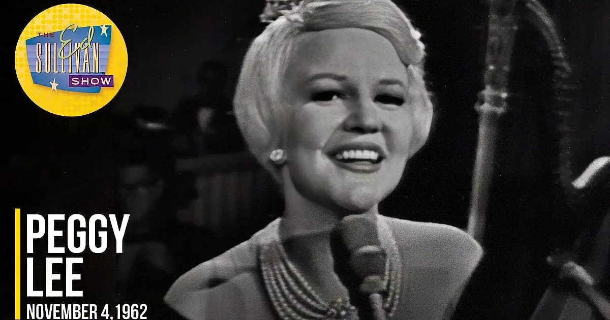 A woman with short hair and pearls sings into a microphone, holding a saxophone, in a black-and-white scene.