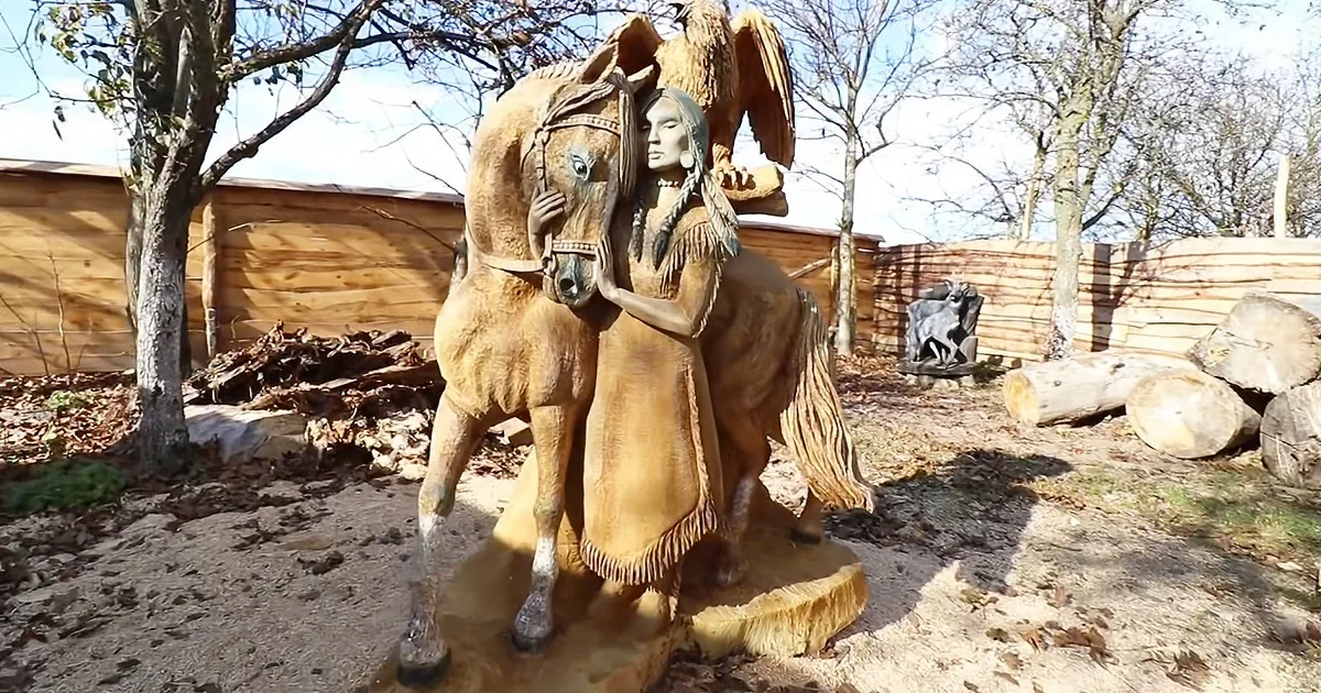 A wooden statue depicts a Native American woman in traditional attire, holding a horse, with an eagle perched on her...