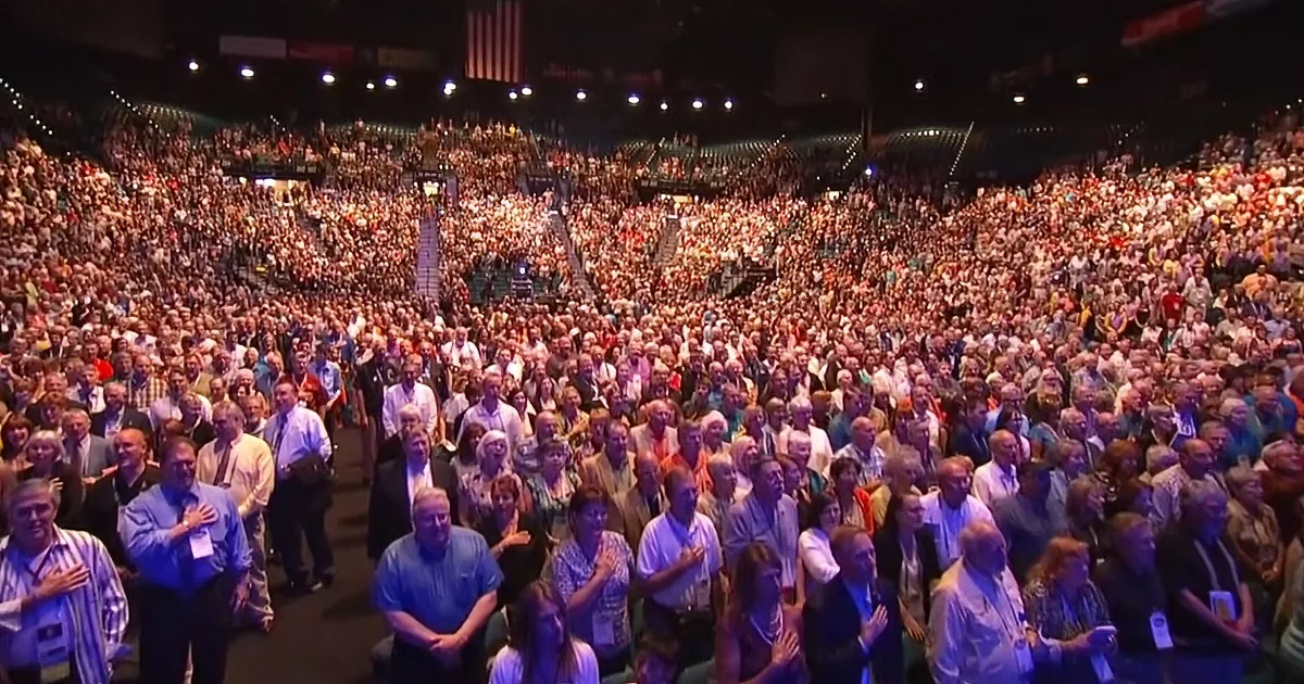 A large crowd of people in a packed arena, some clapping, others watching.