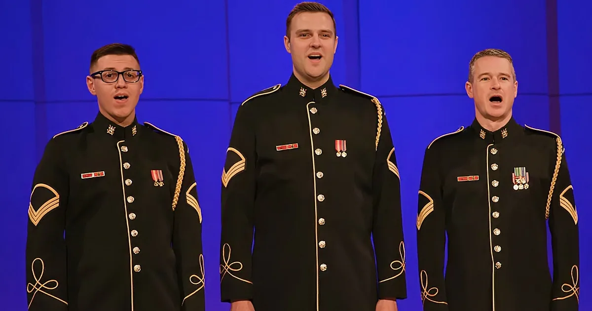 Three men in military uniforms sing on stage, wearing medals and insignia.