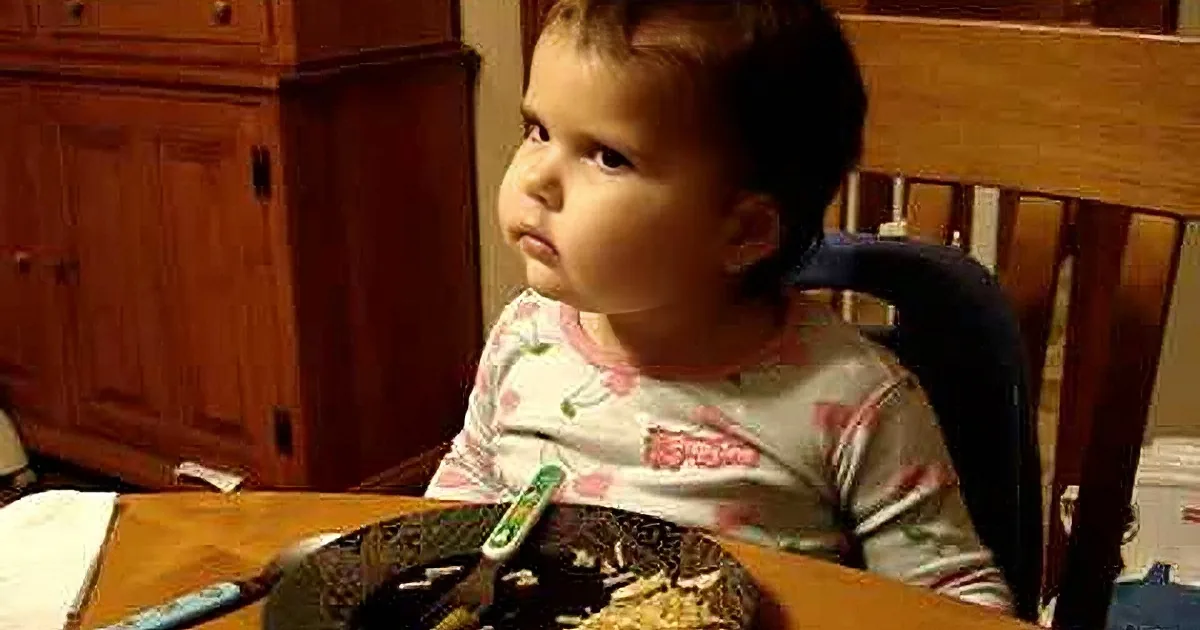A toddler in pajamas sits at a table, leaning forward with hands clasped, appearing contemplative or tired.