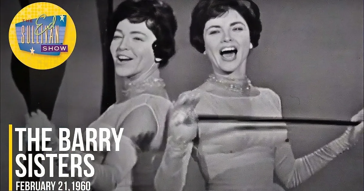 Two women in matching outfits, smiling and holding a baton, appear to be performing or dancing.