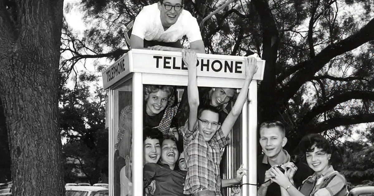 A group of people is joyfully posing in and around a vintage telephone booth.
