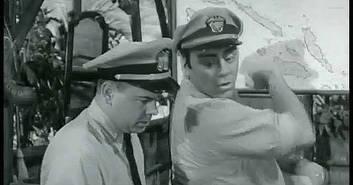Two men in military uniforms, one with a surprised expression, sitting together.