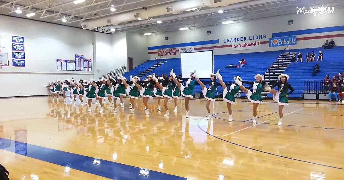 Cheerleaders in green uniforms perform a routine on a basketball court.