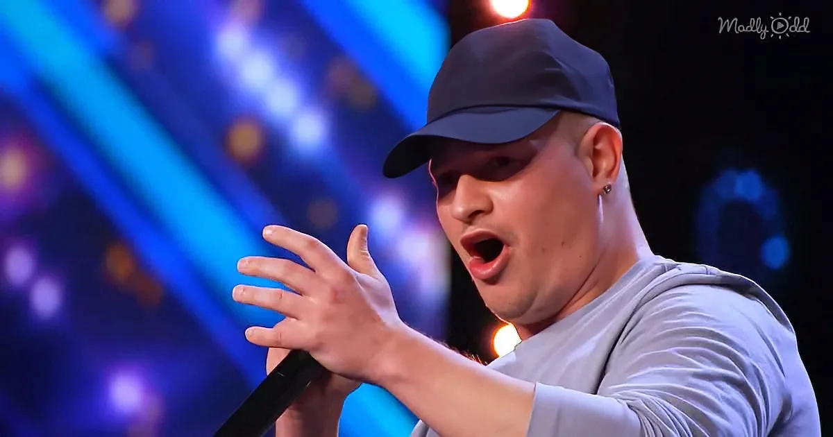A man in a gray shirt and cap sings passionately on stage with a microphone, surrounded by vibrant blue and purple lights.