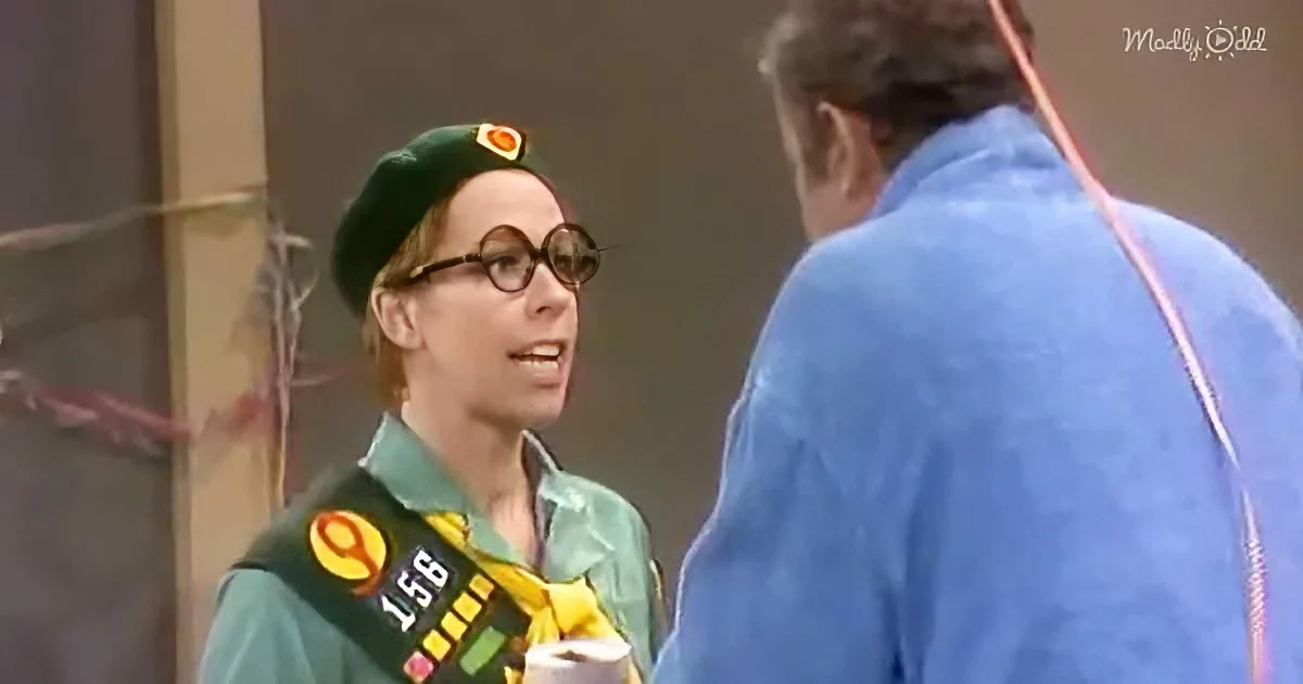 A person in a green uniform with a beret and badge number 158 is talking to another person in a blue outfit.