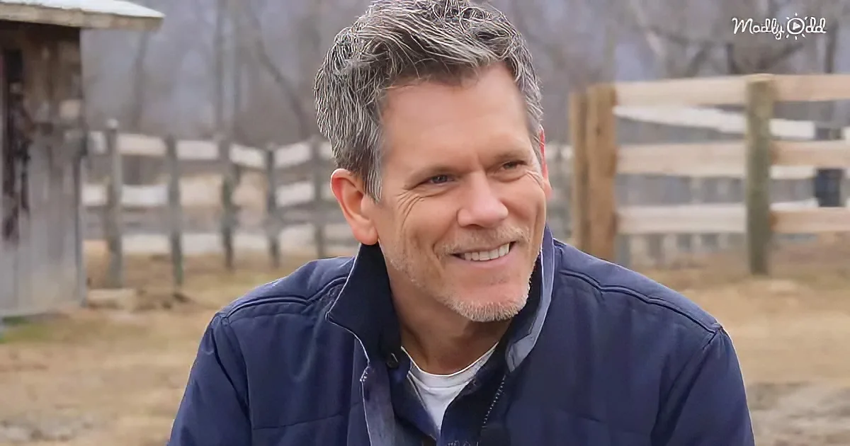 A man with gray hair and a blue jacket smiles in front of a wooden fence and a barn.