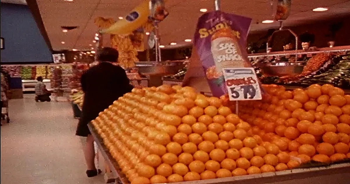 A hand presses buttons on an old cash register, displaying "00.69" and a receipt with grocery items.