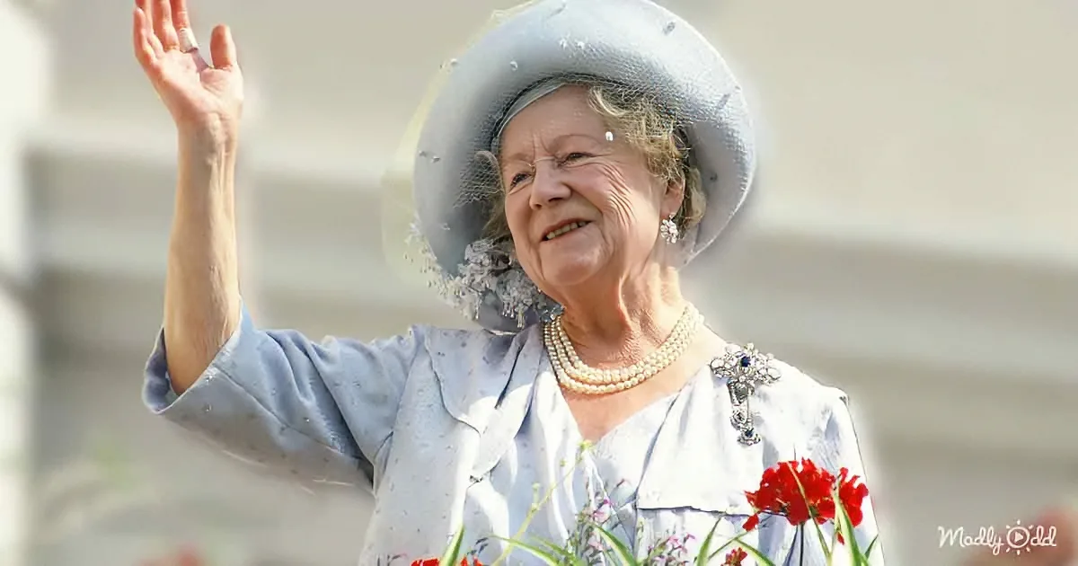 An elderly woman in a light blue outfit and hat waves, adorned with pearls and a brooch, holding flowers.