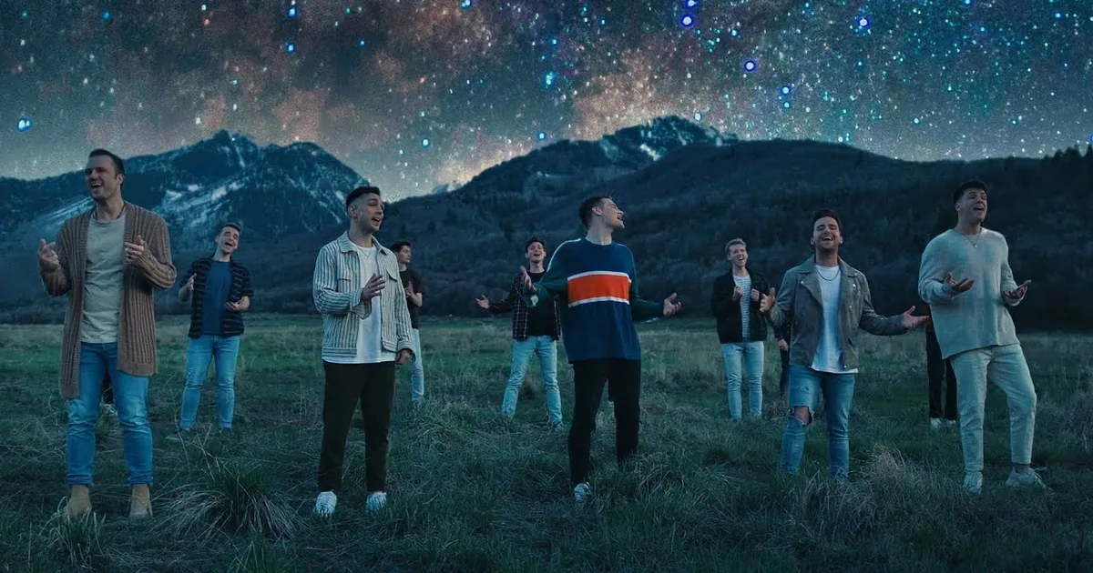 A group of young men stand in a field under a starry sky, with mountains in the background.