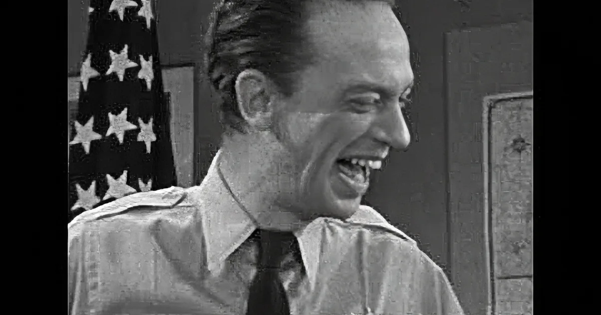 A man in a police uniform appears to be speaking or reacting with a serious expression.